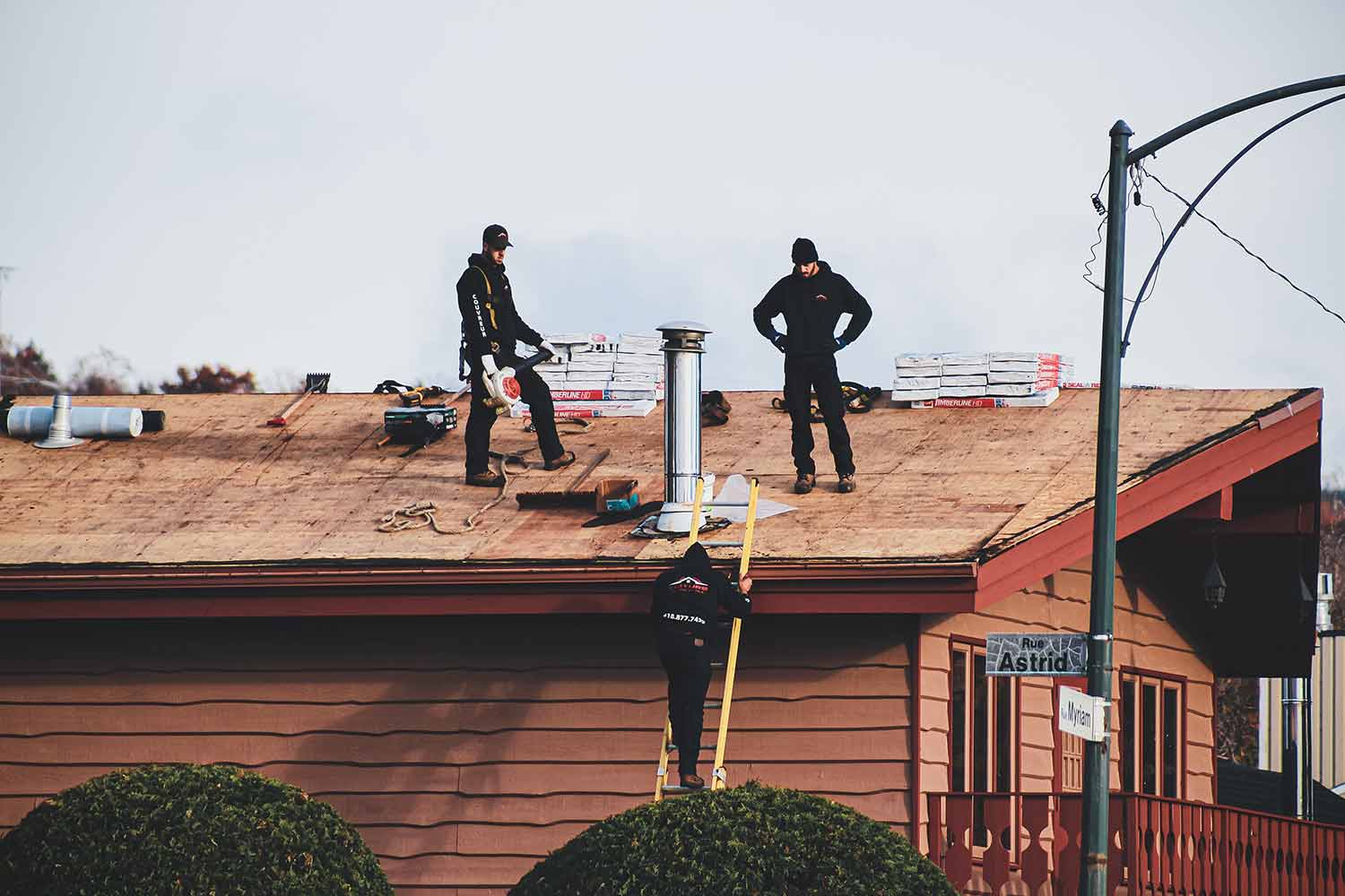 Two Men Standing on A Roof with Another Man on Ladder